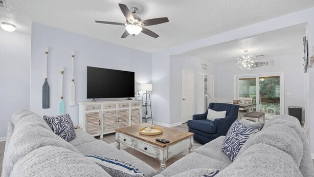A living room with a sofa, armchair, coffee table, TV, and ceiling fan.
