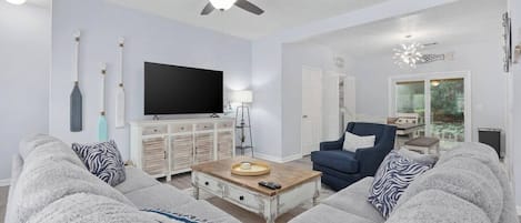 A living room with a sofa, armchair, coffee table, TV, and ceiling fan.
