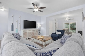 A living room with a sofa, armchair, coffee table, TV, and ceiling fan. - Arcadian Shores Home- Slps 14- 8 beds- retro Games (Myrtle Beach)