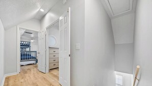 Un couloir avec un lit superposé, une commode et une porte donnant sur une autre pièce.