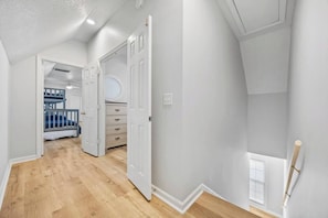 Un couloir avec un lit superposé, une commode et une porte donnant sur une autre pièce.