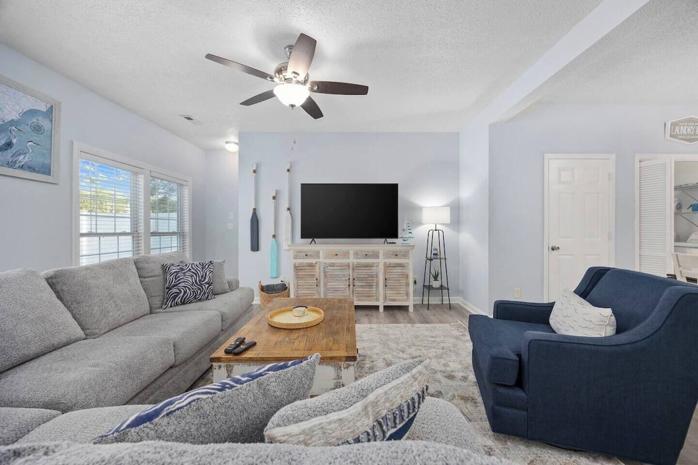 A living room with a sofa, armchair, coffee table, TV, and ceiling fan.