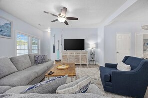 Un salon comprenant un canapé, un fauteuil, une table basse, un téléviseur et un ventilateur de plafond.