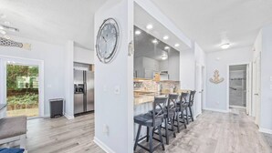 Une cuisine moderne avec un îlot central, des tabourets de bar et une horloge au mur.