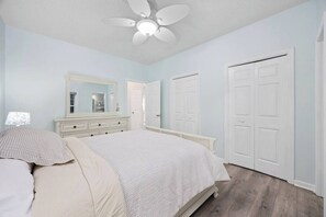 Une chambre à coucher avec un lit, une commode, un miroir, un ventilateur de plafond et des portes blanches.