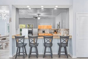 Une cuisine moderne dotée d’un coin bar, avec un ventilateur de plafond, des appareils électroménagers intégrés et une grande fenêtre.