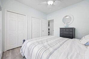 Une chambre à coucher avec un lit, une commode, un ventilateur de plafond et une porte.