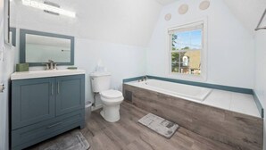 A bathroom with a bathtub, toilet, vanity, and a window.