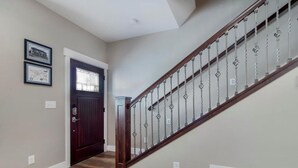 Un couloir avec un escalier en bois, une porte sombre et deux tableaux encadrés accrochés au mur.