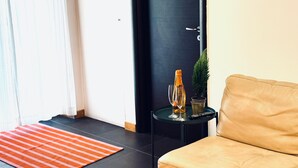 Una sala de estar moderna con un sofá beige, una mesita auxiliar con un control remoto, una planta en maceta y una botella de vidrio.