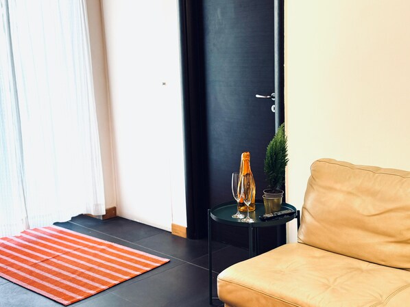 A modern living room with a beige sofa, a small side table with a remote control, a potted plant, and a glass bottle. - Casa Claudia (Salerno)