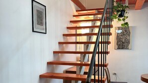 Una escalera de madera con barandilla metálica, una planta en maceta y un cuadro en la pared.