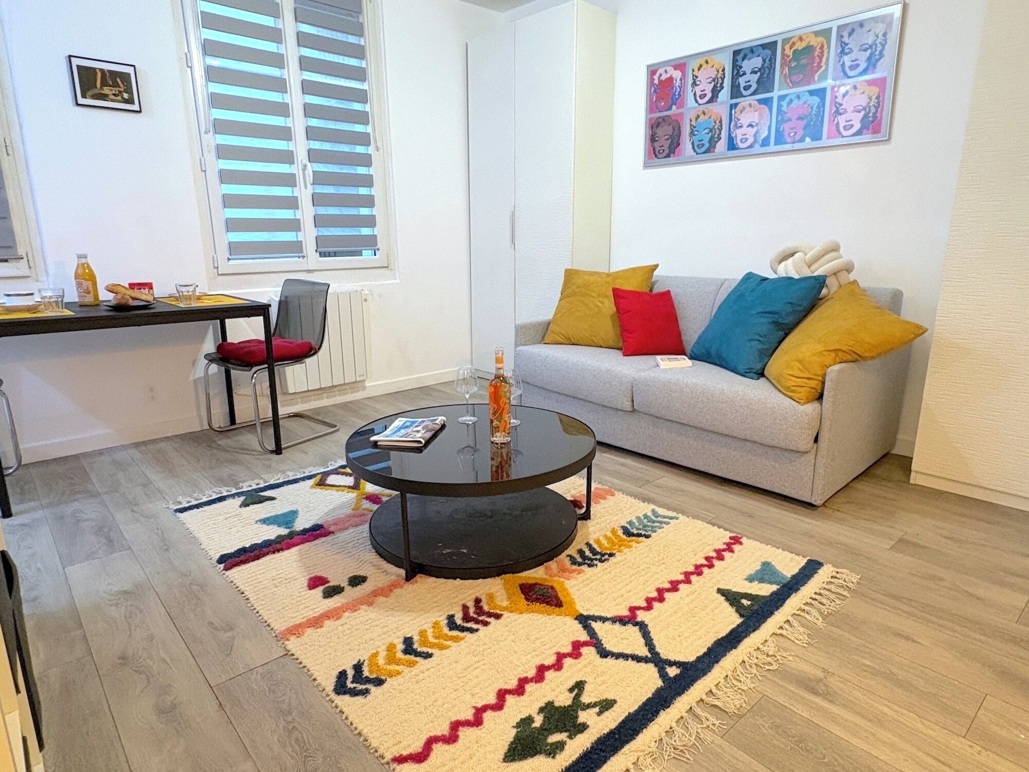 Ein modernes Wohnzimmer mit einem grauen Sofa, bunten Kissen, einem schwarzen Couchtisch und einem gemusterten Teppich.