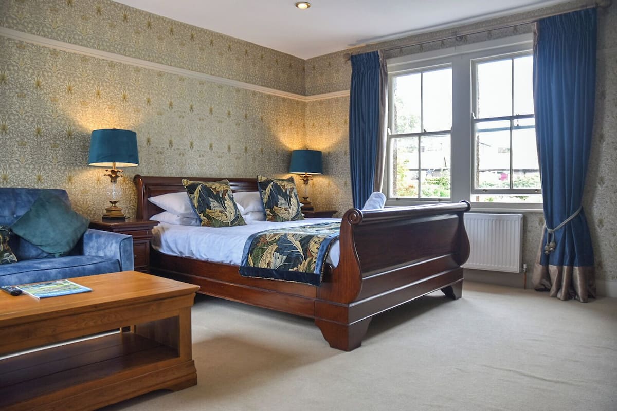 A bedroom with a large bed, a wooden nightstand, a blue sofa, and a wooden coffee table.