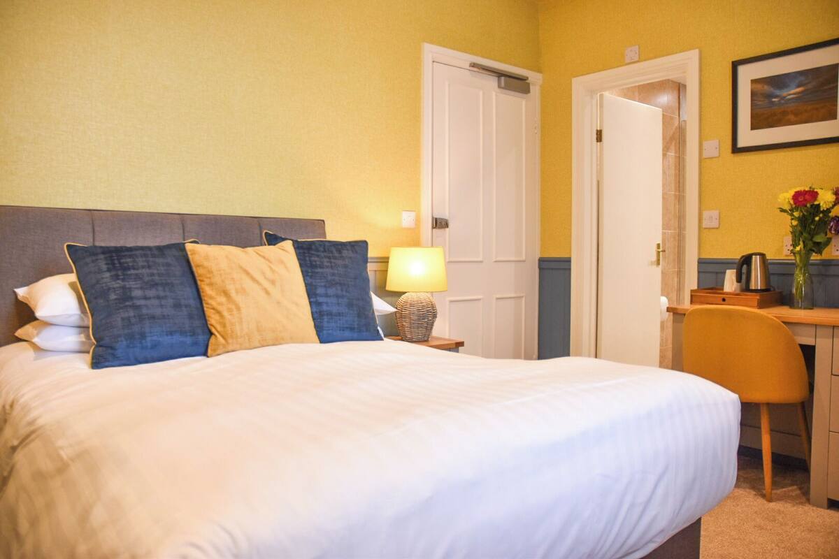 A hotel room with a large bed, a desk, a chair, and a door.