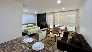 Una habitación de hotel moderna con una cama, un escritorio pequeño con una silla, un sofá y un área de comedor con mesa y sillas.
