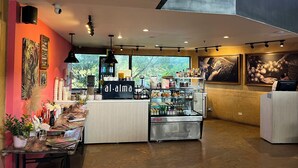 Un interior de cafetería con mostrador, estantes llenos de bebidas y obras de arte en las paredes.