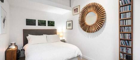 Une chambre avec un grand lit, une bibliothèque en bois et un miroir rond accroché au mur.