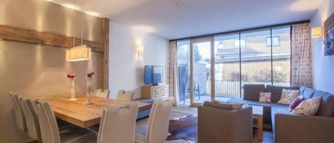 Un salon moderne avec une table à manger en bois, des chaises grises, un canapé et un téléviseur.