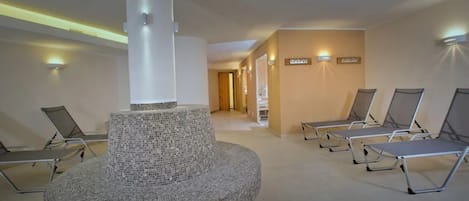 Un espacio de spa con una fuente de mosaico central, sillones de descanso y un pasillo que conduce a una puerta.