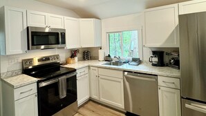 A modern kitchen with white cabinets, stainless steel appliances, and a wooden floor.