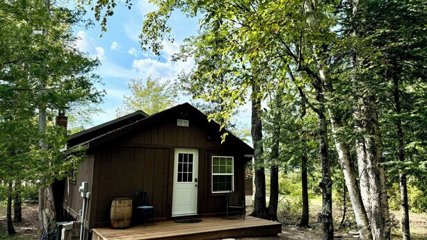 A rustic cabin with a wooden deck, a white door, and a window.