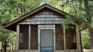 A small wooden cabin with a blue door, surrounded by trees.