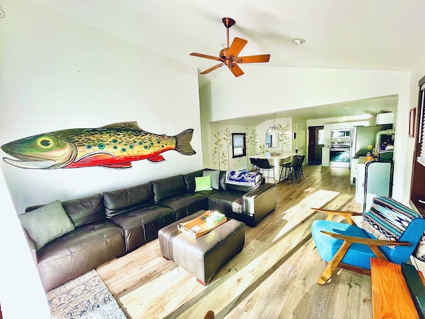 A living room with a large fish mural, a ceiling fan, a sofa, a coffee table, and a kitchen in the background.