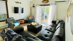 A living room with a black leather sofa, a wooden ceiling fan, a flat-screen TV, and a large window with curtains.