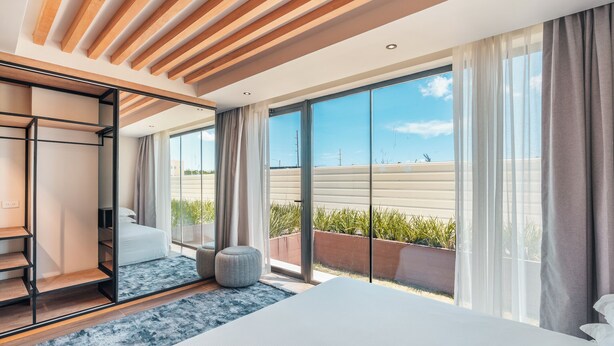 A modern bedroom with a large bed, a built-in wardrobe, and a sliding glass door leading to a balcony. - Probar Suites Punta Cana (Punta Cana)