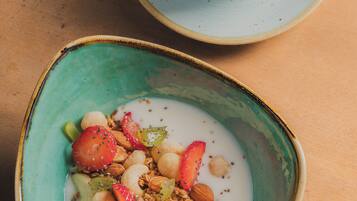Mesa de café da manhã com xícara de café e tigela de iogurte com frutas e granola.
