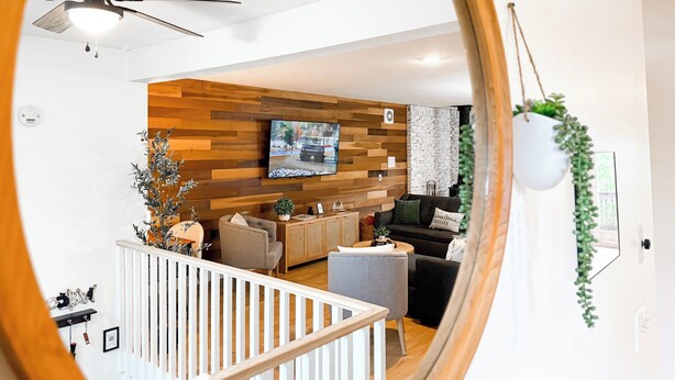 A modern living room with a wooden wall panel, a ceiling fan, a flat-screen TV, and a staircase leading to an upper level. - Perfect Summer Getaway-Near Storyland (Bartlett)