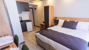 A modern hotel room with a large bed, a small kitchenette, and a separate seating area with a table and chairs. - Çamlıca Park Otel (Of)