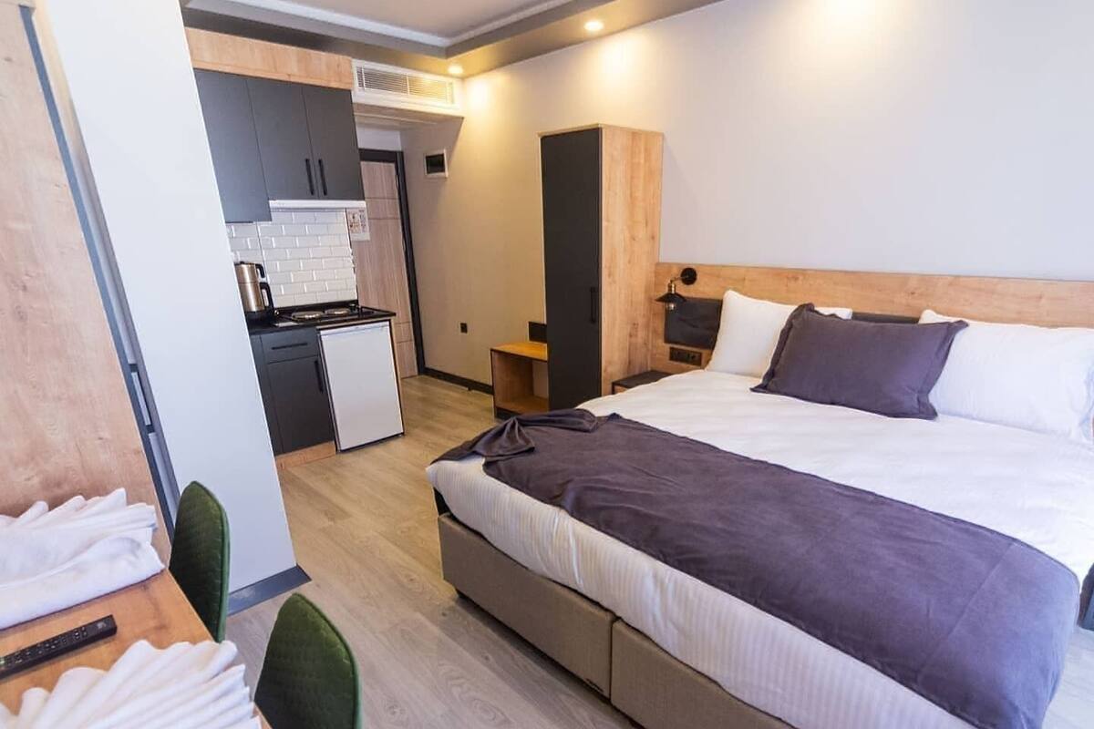 A modern hotel room with a large bed, a small kitchenette, and a separate seating area with a table and chairs.