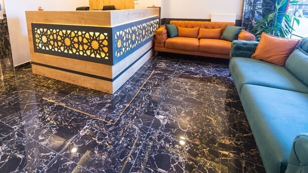 A reception area with a wooden desk, a sofa, and a TV on the wall. - Çamlıca Park Otel (Of)