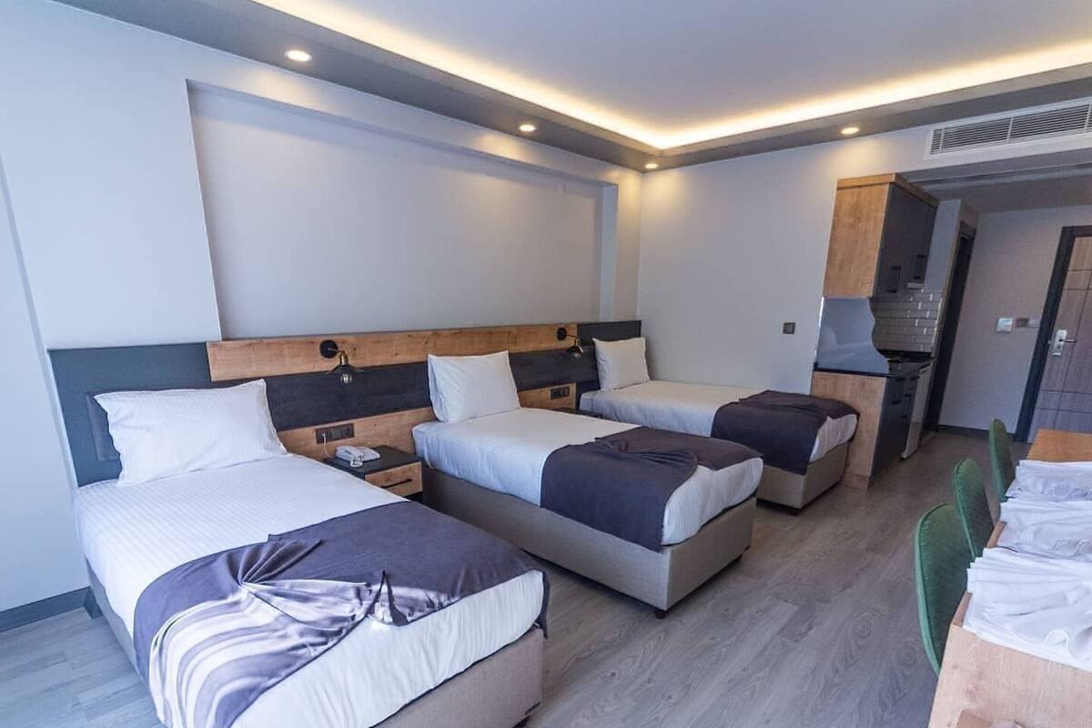 A modern hotel room with three beds, a kitchenette, and a dining area.