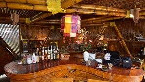A bar area with a curved wooden bar, wicker chairs, a hanging lantern, and various bottles and glasses on the counter. - An's Space Sapa (Sa Pa)