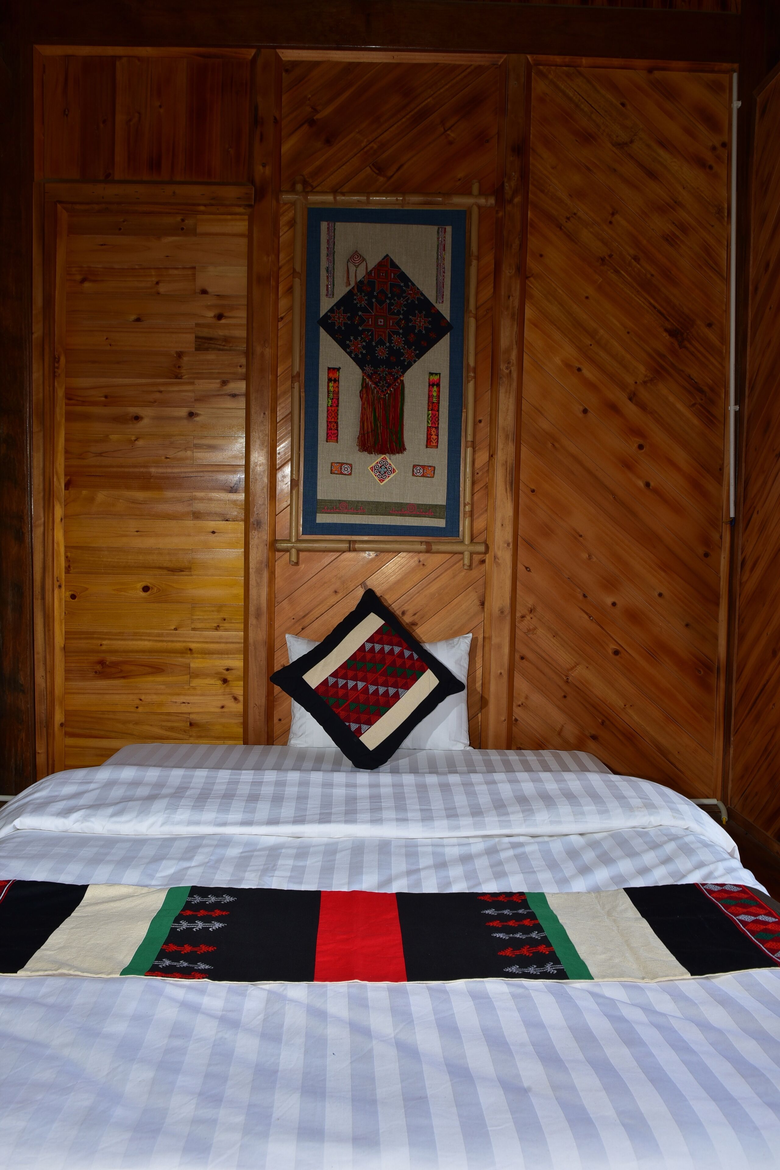 A wooden cabin room with a bed, a quilt, and a framed picture on the wall.