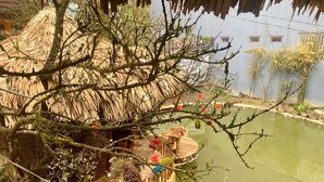 A thatched-roof structure with a wooden deck over water, surrounded by greenery and potted plants. - An's Space Sapa (Sa Pa)
