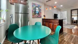 Una cocina moderna con un refrigerador de acero inoxidable, sillas de comedor color turquesa y un mural colorido en la pared.