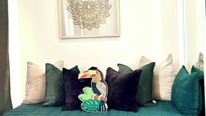 Un sofá color turquesa con un cojín decorativo, una obra de arte enmarcada en la pared y piso de madera.