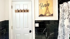 Un baño con una puerta blanca, un toallero de pared, un cuadro enmarcados de la Torre Eiffel, baldosas de mármol negro y una cortina de ducha con estampado floral.
