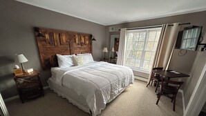 Une chambre à coucher avec un grand lit, une tête de lit en bois, un bureau et une fenêtre avec des rideaux.