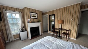 A hotel room with a bed, a fireplace, a desk with two chairs, a window with curtains, and a door. - The Bond Inn Room #9 (Warrensburg)