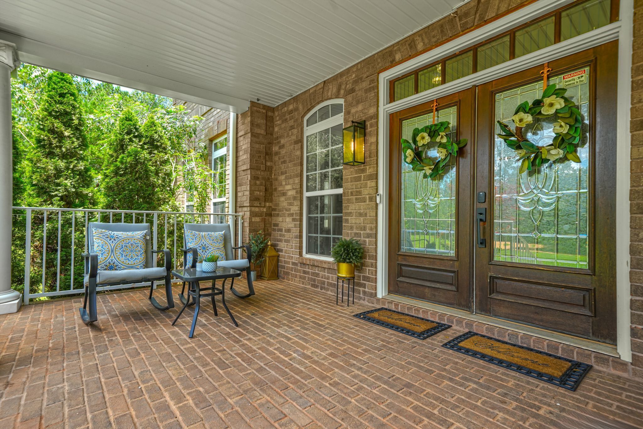 A covered porch with brick flooring, two rocking chairs, and a small table.