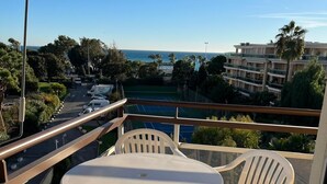 A balcony with a round table and four chairs, overlooking a tennis court and a pool, with buildings and palm trees in the background.