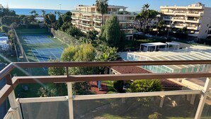A balcony with a view of a tennis court, a pool, and surrounding buildings.