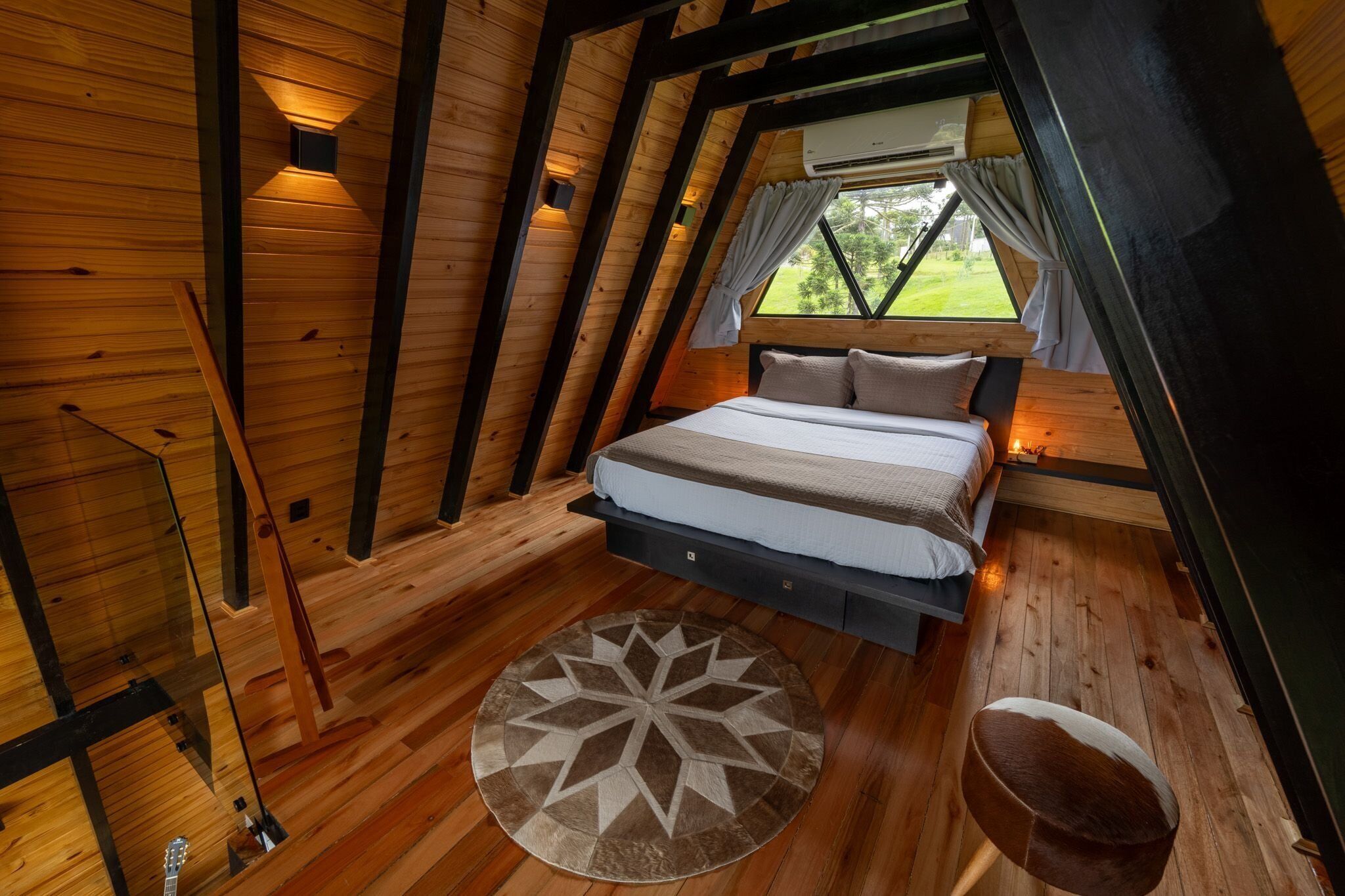 A cozy attic bedroom with a bed, a round rug, and a wooden floor.
