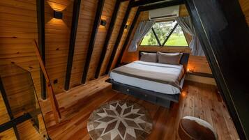 A cozy attic bedroom with a bed, a round rug, and a wooden floor.