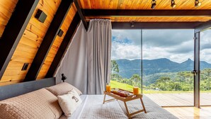 Ein Schlafzimmer mit einem großen Bett, einer Holzbalkendecke und Bergblick durch eine Glastür.
